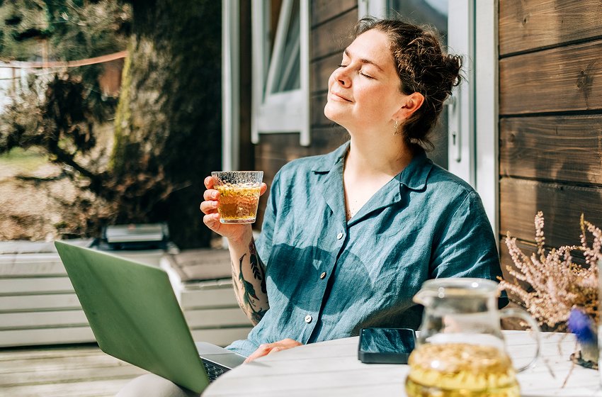 A woman sitting outside with a laptop and an iced beverage.